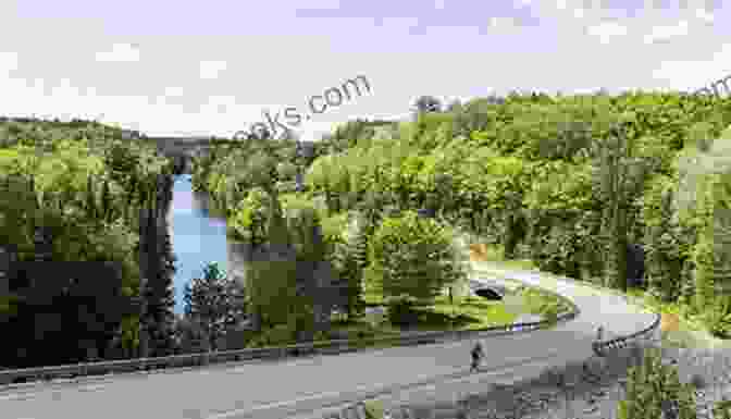 A Cyclist Riding Through The Muskoka Lakes Trail, Surrounded By Towering Granite Cliffs And Sparkling Waters, With A Stunning Reflection Of The Landscape In The Water. Cycling In Central Ontario Elaine Bertolotti